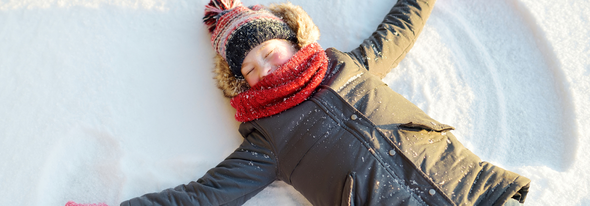 Person making a snow angel. They are wearing a grey jacket, red gloves, red scarf and a red hat.